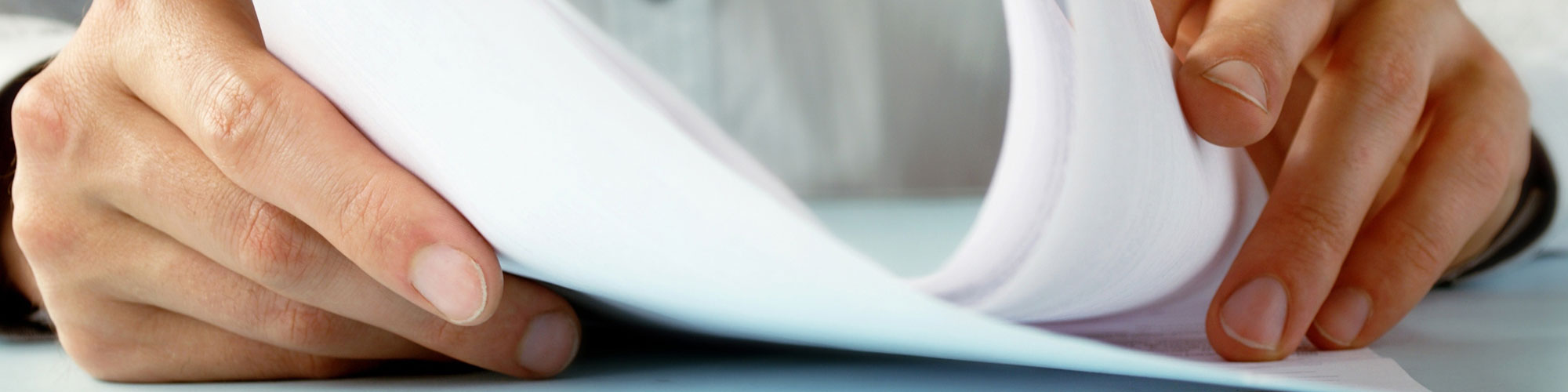 Hands flipping through sheets of paper on a flat surface, suggesting an act of reviewing or organizing documents, relevant to document management.